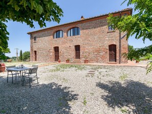 A stone building with a gravel courtyard, a table with chairs, and potted plants.