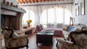 A cozy living room with a fireplace, floral armchairs, a sofa, and a wooden ceiling. - Tuscan Farmhouse in Peccioli with Swimming Pool near Lakes (Peccioli)