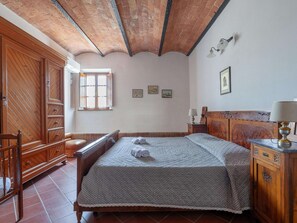 A bedroom with a wooden bed, a wooden wardrobe, a wooden bench, and a window with curtains.