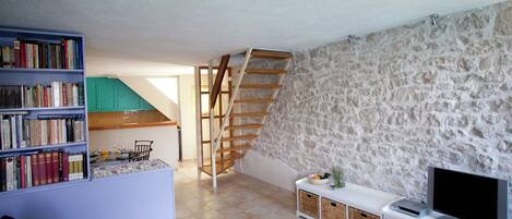 A living room with a bookshelf, a glass coffee table with flowers, a TV, and a stone wall.