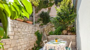 A stone-walled outdoor patio with a table set for two, surrounded by greenery and a stone wall. - Beautiful Holiday Home on the Island Brac, With the Sea and a Small Beach in Front of the Door (Pucisca)