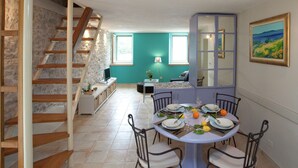 A dining area with a table set for four, a staircase, and a view of the kitchen. - Beautiful Holiday Home on the Island Brac, With the Sea and a Small Beach in Front of the Door (Pucisca)
