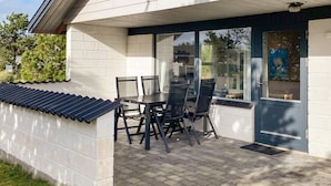 A covered patio with a table and chairs, a door with a poster, and a brick wall. - 6 Person Holiday Home in Thisted (Thisted)
