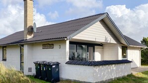 A single-story building with a sloped roof, a chimney, and a small porch area. There are three trash bins outside, and a sign with the number "3" on the building. - 6 Person Holiday Home in Thisted (Thisted)