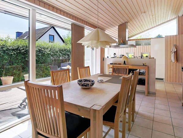Una cocina moderna con armarios de madera, una mesa de comedor con sillas y un amplio ventanal con vistas a un jardín.