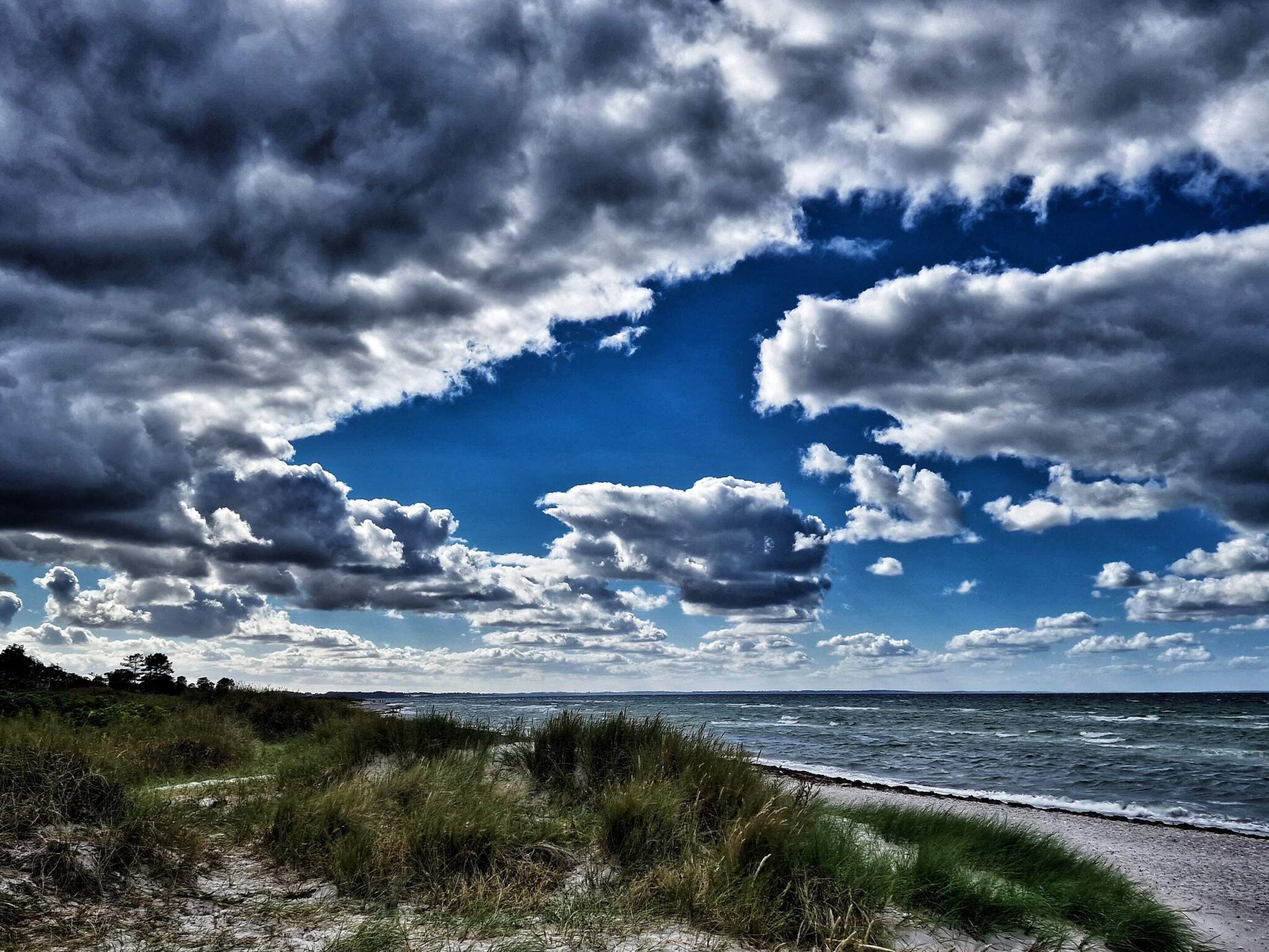 A beach with a grassy foreground and a view of the ocean under a partly cloudy sky.