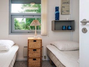 A bedroom with two single beds, a window with a view of greenery, a lamp on a wooden stand, and a shelf with a blue mug and a star-patterned mug. - 6 Person Holiday Home in Skovgårde Allingåbro (Allingåbro)