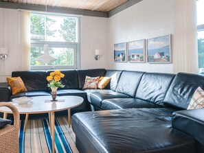 A modern living room with a black leather sofa, a round coffee table, and a vase of flowers. There are three framed pictures on the wall and a window with a view of trees. - 6 Person Holiday Home in Skovgårde Allingåbro (Allingåbro)