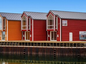 A row of red buildings with large windows and a metal roof, adjacent to a body of water. - 8 Person Holiday Home in Sandoy (Ålesund)