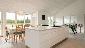 A spacious kitchen with a large island, ample natural light, and a dining area with wooden chairs. - Holiday Home in Jerup (Jerup)
