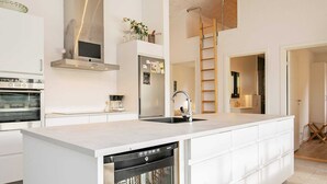 A modern kitchen with white cabinetry, a stainless steel dishwasher, a built-in oven, and a refrigerator. - Holiday Home in Jerup (Jerup)