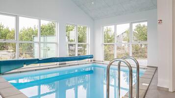 Una piscina interior con ventanas amplias, borde azul y barandillas de metal.