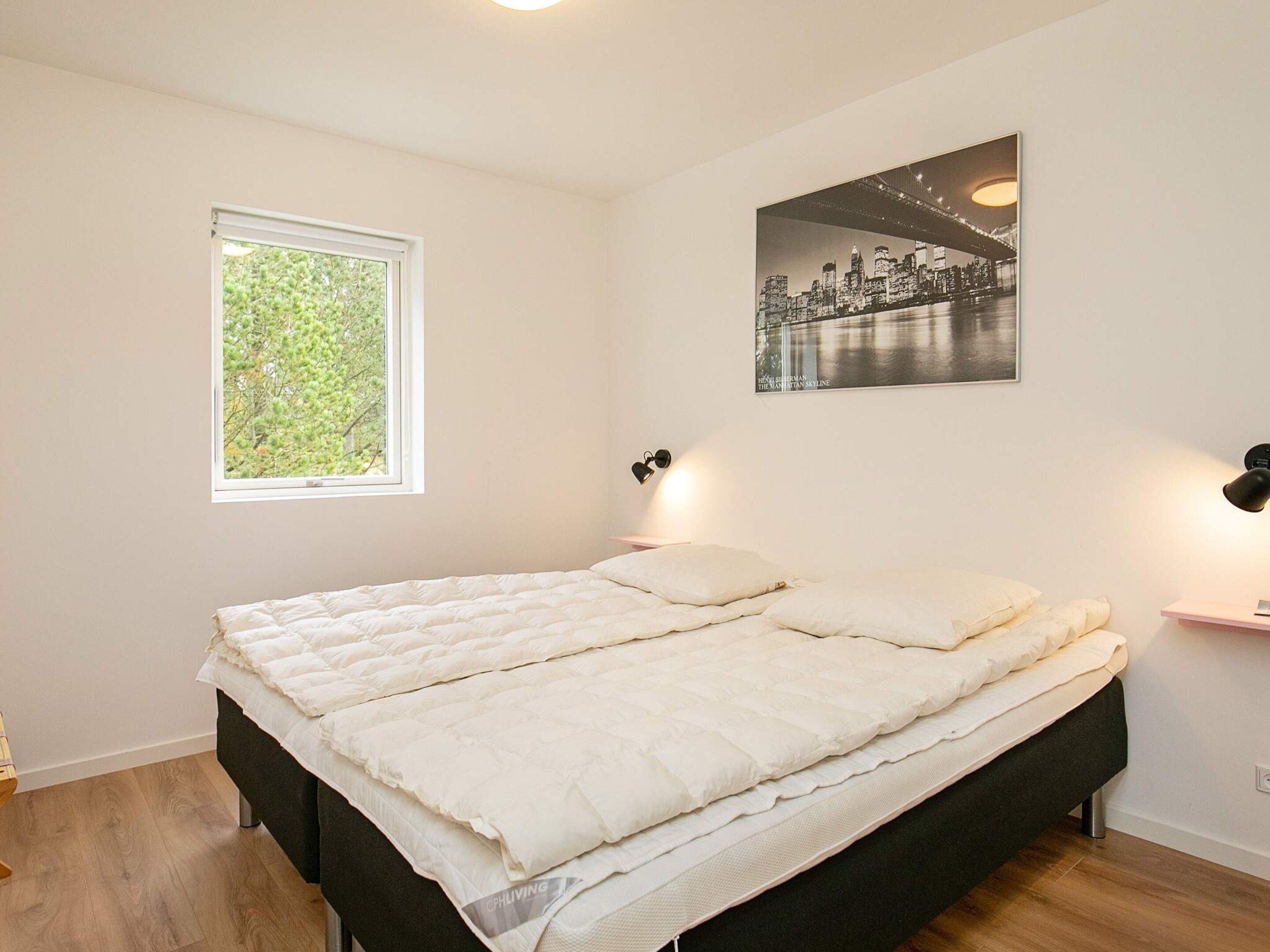 A bedroom with a bed, a window, a wall-mounted picture, and a bedside table.