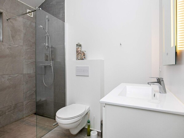 A modern bathroom with a glass shower enclosure, a white toilet, and a sink with a mirror.