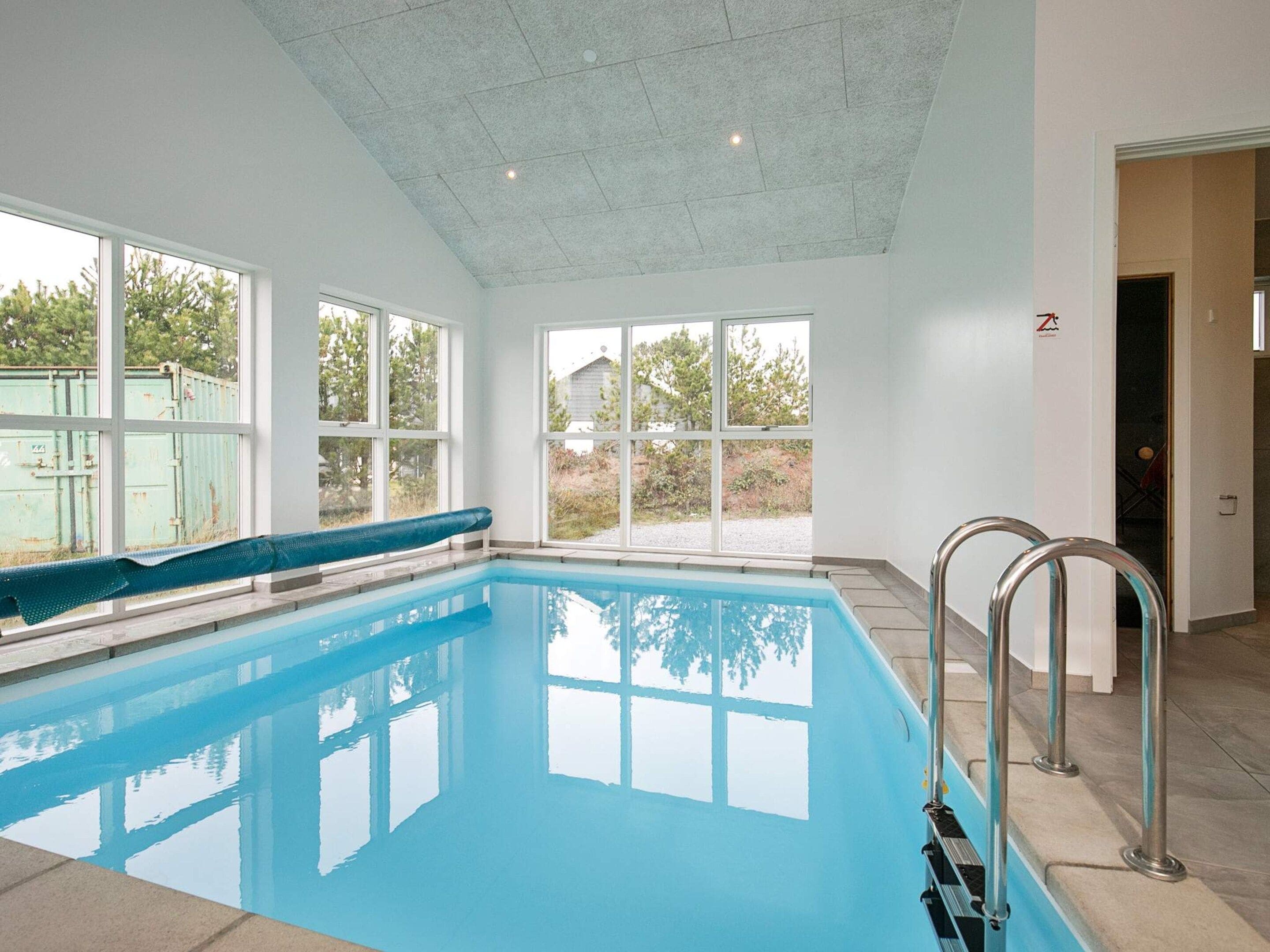 Una piscina interior con ventanas amplias, techo de azulejos y barandilla de metal.