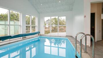 Una piscina interior con ventanas amplias, techo de azulejos y barandilla de metal.
