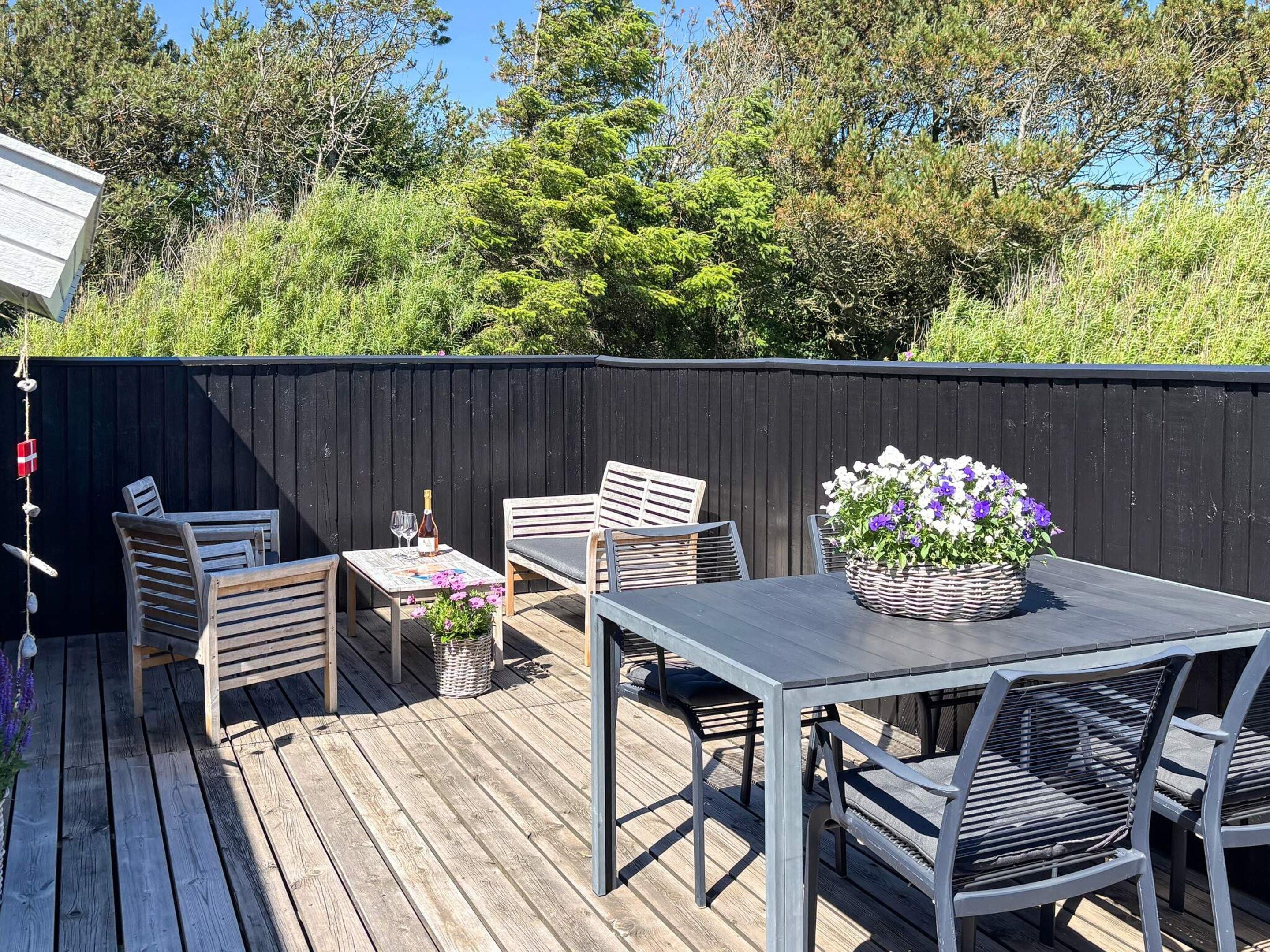 A wooden deck with a table and chairs, a bottle of wine, and a basket of flowers.