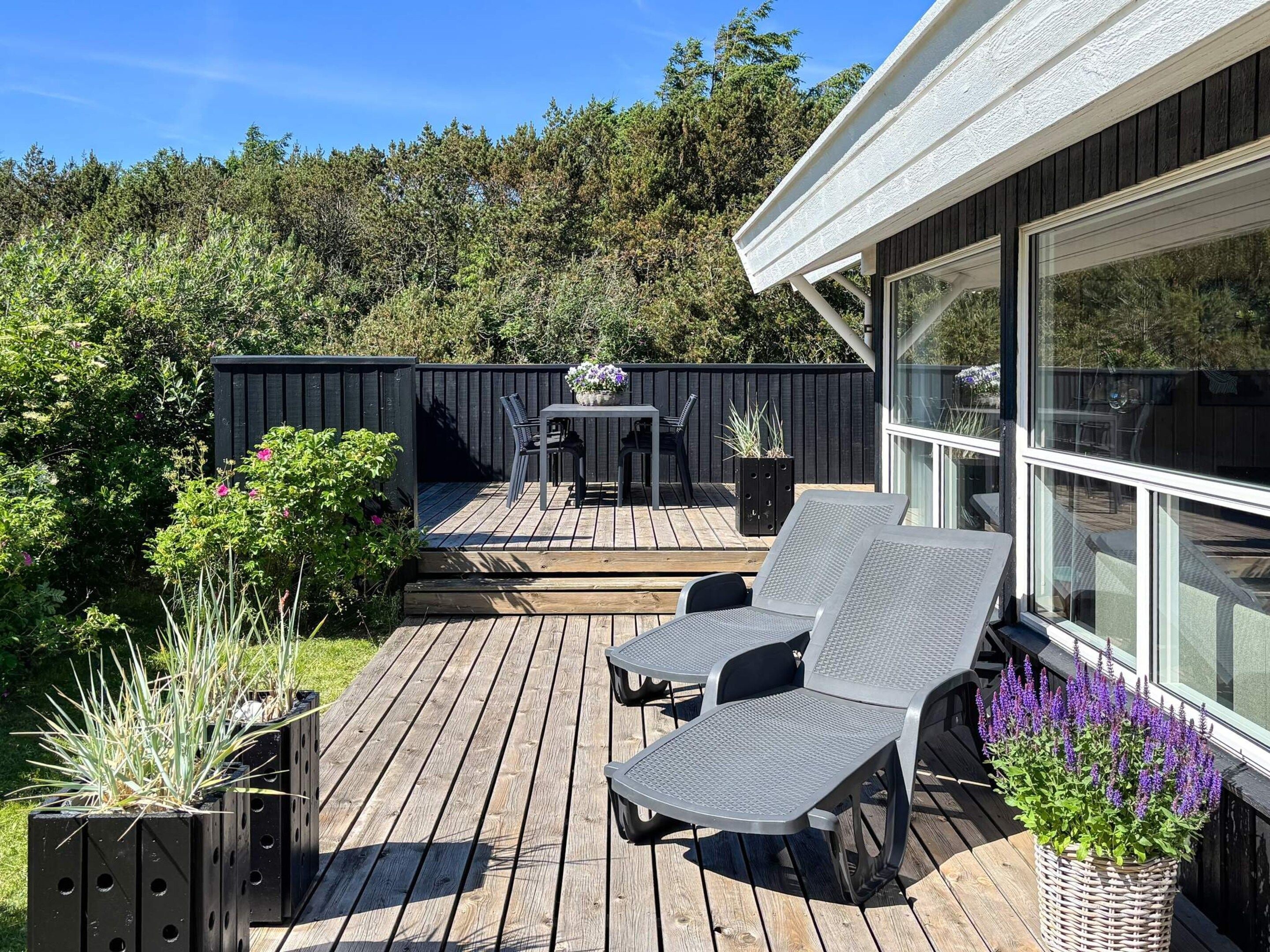 A wooden deck with two lounge chairs, a table, and potted plants.