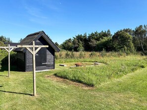 A rustic wooden cabin with a sloped roof, surrounded by a well-maintained grassy area and dense trees in the background. - Holiday Home in LÃ¸kken (Lokken)