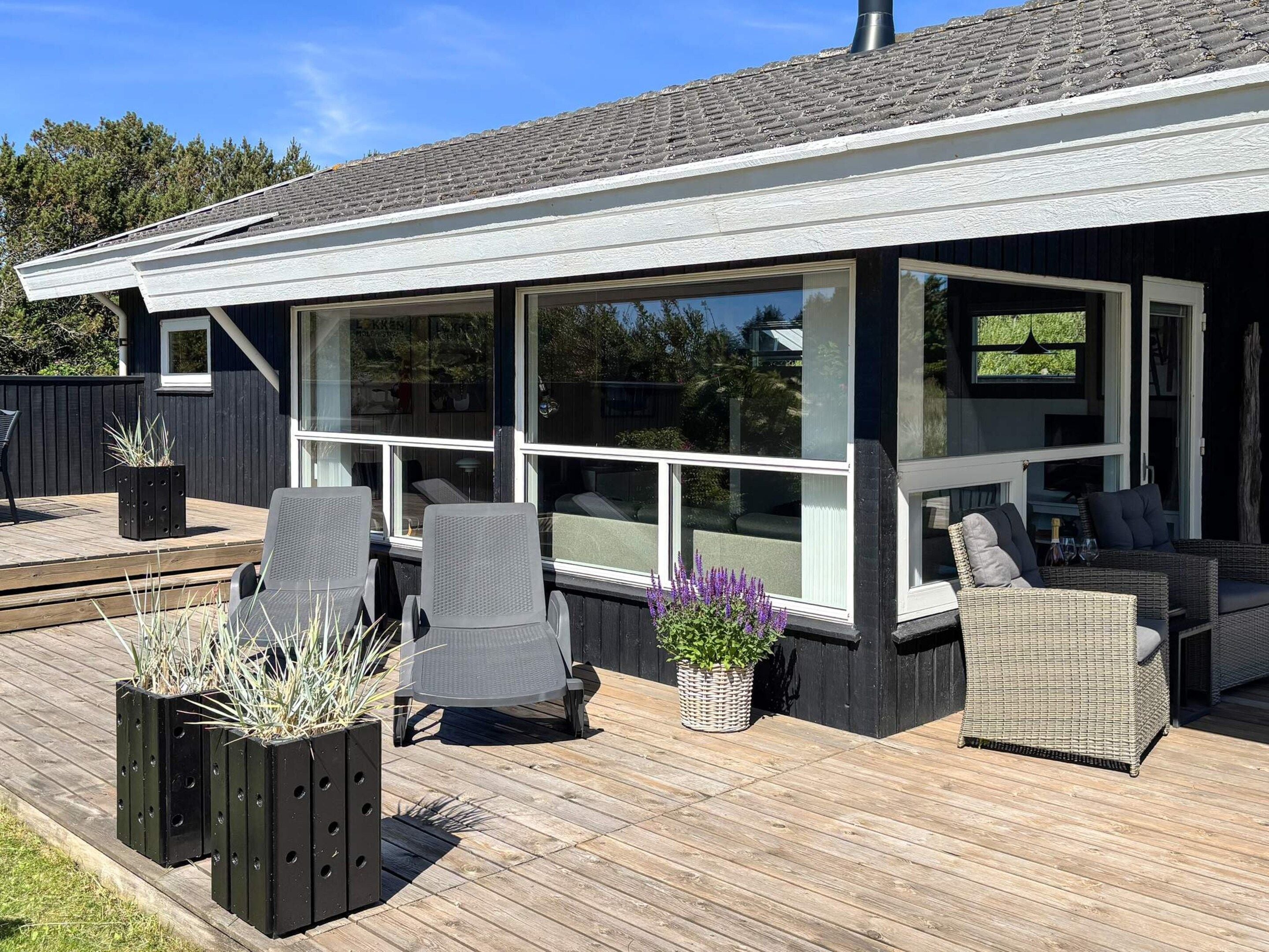 A covered outdoor seating area with chairs and tables, large windows, and potted plants.