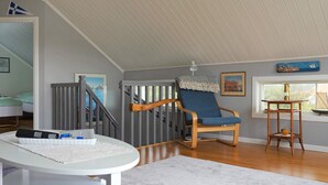 A room with a wooden chair, a white desk, a window with a view, and a staircase.
