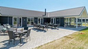 A modern building with a tiled roof, outdoor seating area, and a covered patio. - Holiday Home in Nørre Nebel (Norre Nebel)