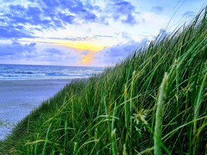 A beach with grass in the foreground and a sunset in the background. - Holiday Home in Nørre Nebel (Norre Nebel)
