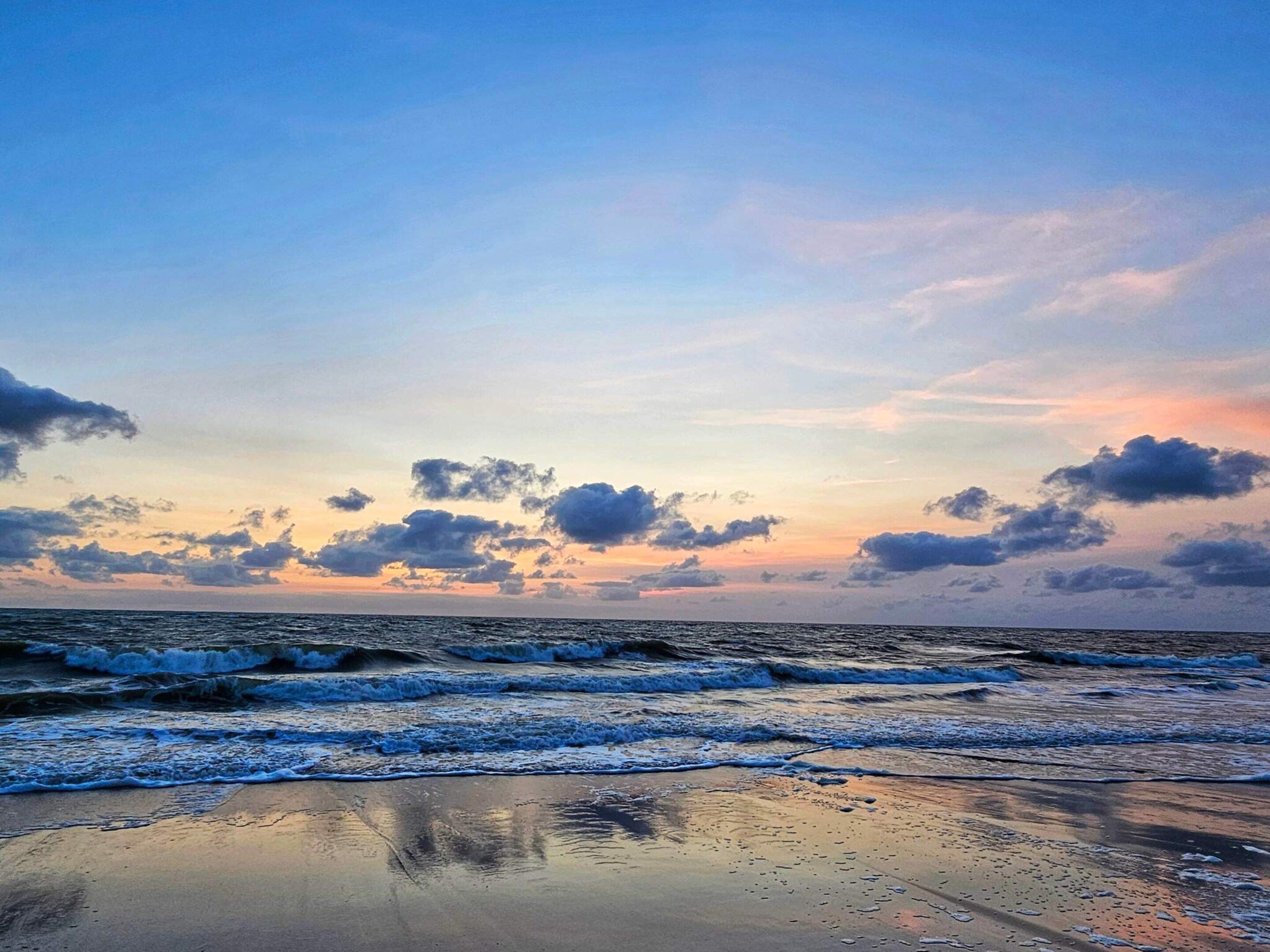A beach with waves and a sunset sky.