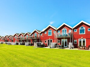 A row of red buildings with balconies, a grassy lawn, and a clear blue sky.