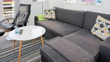 A modern living room with a grey sofa, a black leather chair, a white coffee table, and a striped rug. There are two artworks on the wall and a window with a view of a red building.