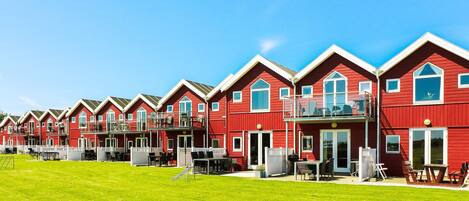 A row of red buildings with balconies, a grassy lawn, and a clear blue sky.