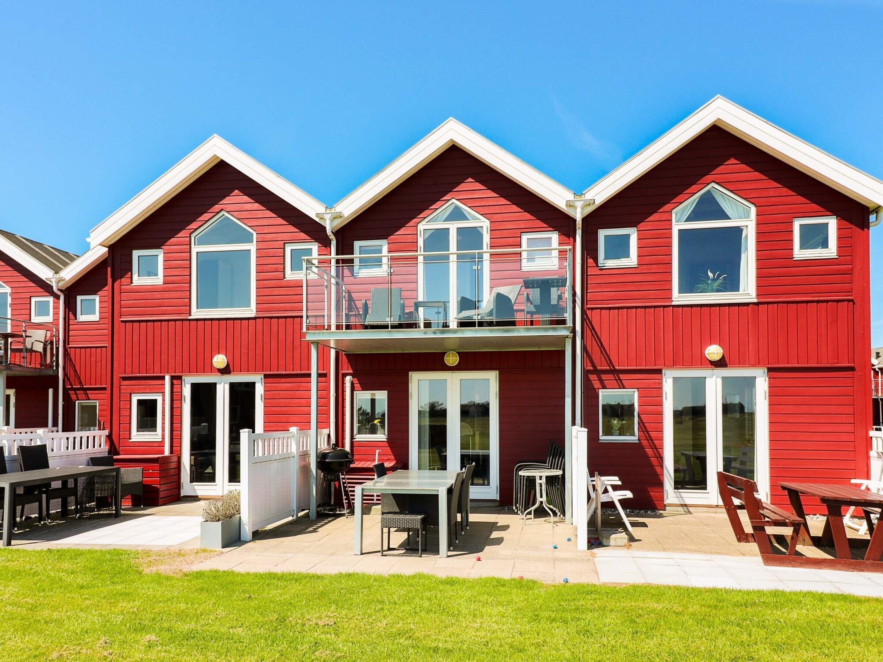 En rød bygning med balkon, udendørs siddepladser og en klar himmel.
