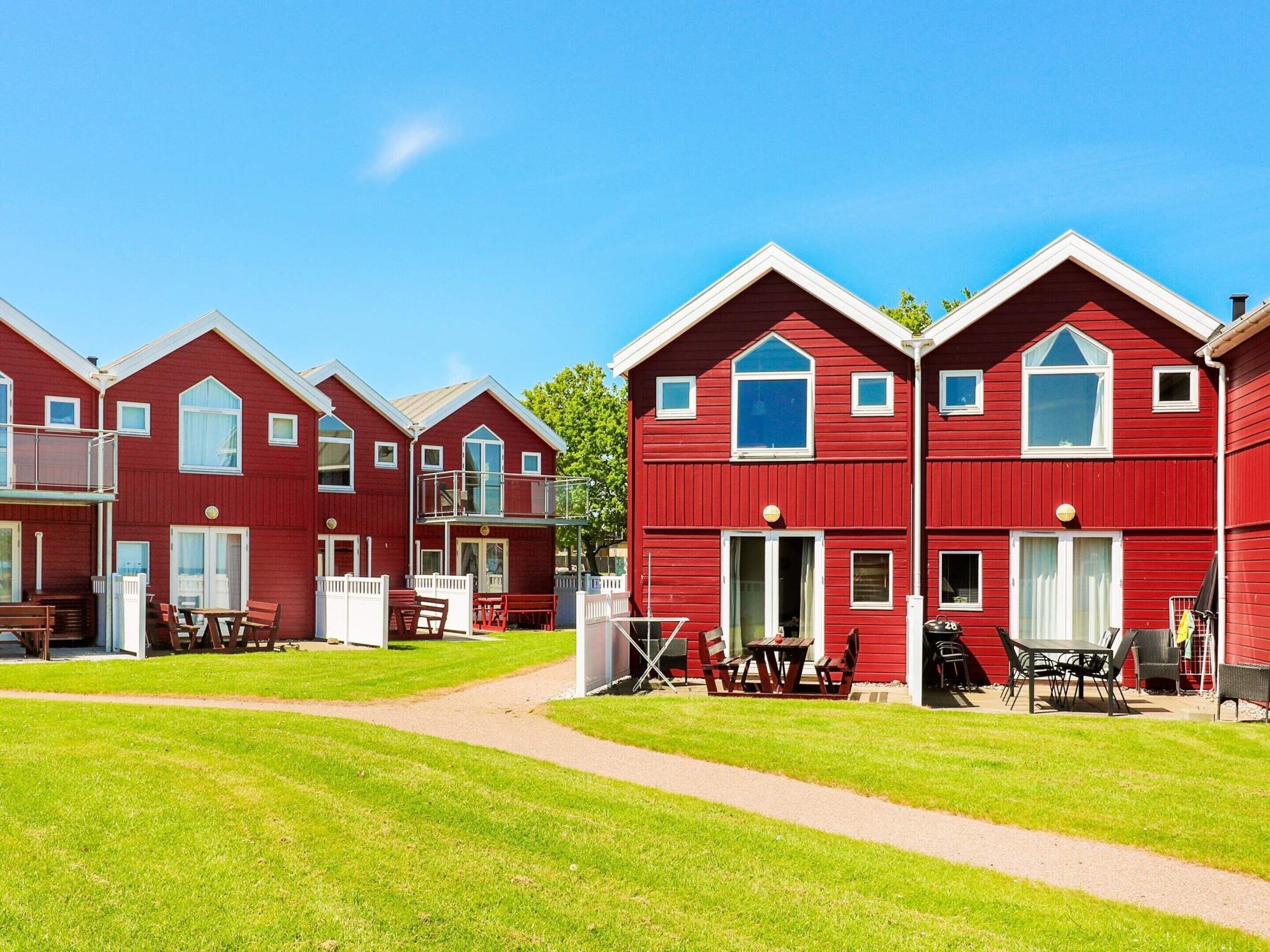 A row of red buildings with balconies, a grassy lawn, and outdoor seating areas.