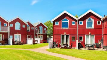 A row of red buildings with balconies, a grassy lawn, and outdoor seating areas.