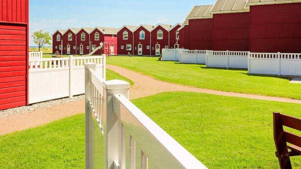 A row of red barns with white fences, a clear sky, and a grassy area.