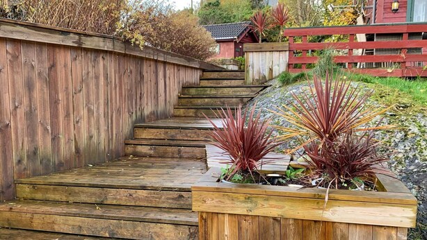 A wooden staircase leading up to a red building, surrounded by plants and a wooden fence. - 6 Person Holiday Home in Bomlo (Bomlo)