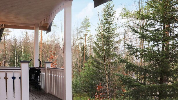 Een overdekte veranda met een witte balustrade, omringd door bebossing.