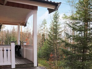 Eine überdachte Veranda mit weißer Reling, umgeben von einem Waldgebiet.