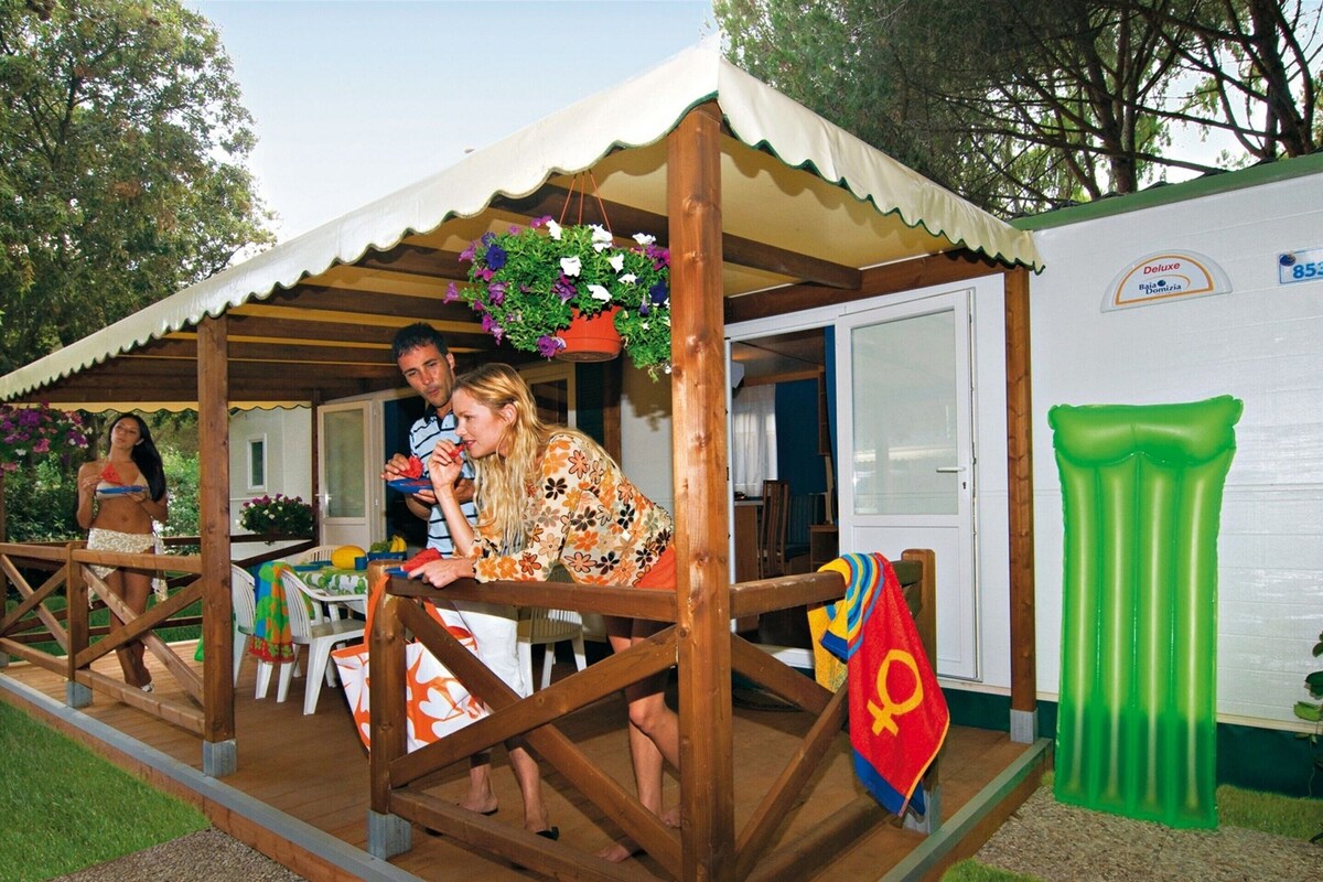 Une terrasse en bois avec un espace salon couvert, une piscine gonflable verte et un bâtiment blanc avec une enseigne.