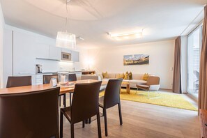 Een moderne woonkamer met een bank, salontafel en een eethoek. Er is een keuken met kastjes en een magnetron.