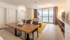 Una camera d'albergo moderna con zona pranzo, divano con cuscini, televisione e vista sull'oceano.