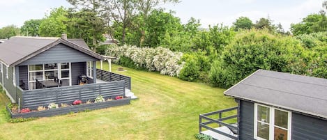 A two-story cabin with a deck, surrounded by a well-maintained lawn and dense greenery.
