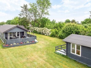 A two-story cabin with a deck, surrounded by a well-maintained lawn and dense greenery.