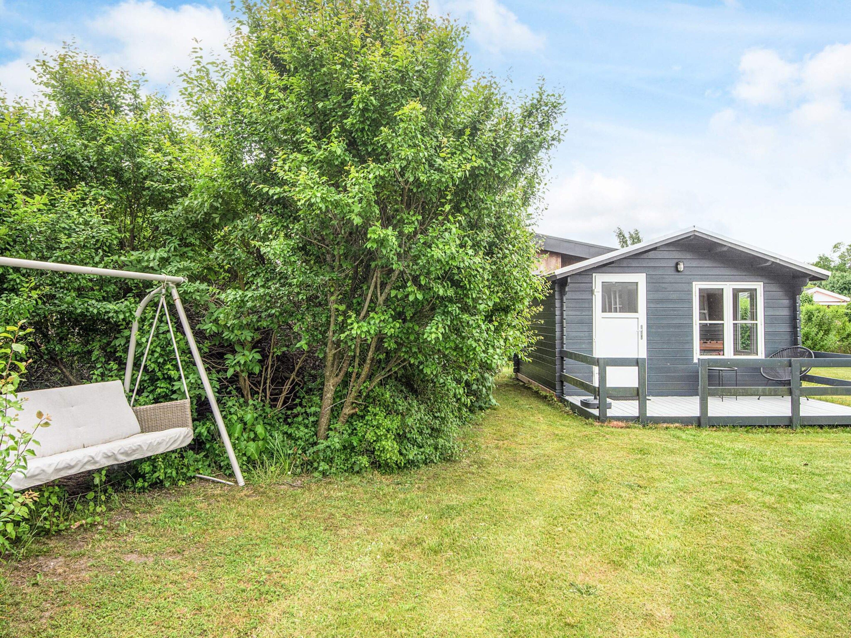 A small cabin with a porch, surrounded by lush greenery and a swing set.