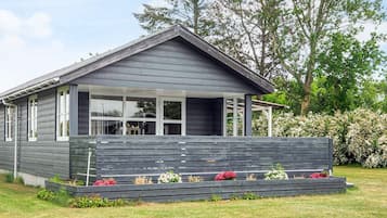 A modern house with a porch, large windows, and a garden with flowers.