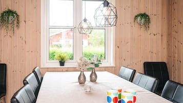 Uma área de refeições com parede revestida em madeira, uma janela grande, duas luminárias pendentes e uma mesa com cadeiras e objetos decorativos.