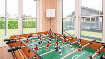 A foosball table with a wooden table and a green playing surface, set in a room with large windows and a white ceiling.