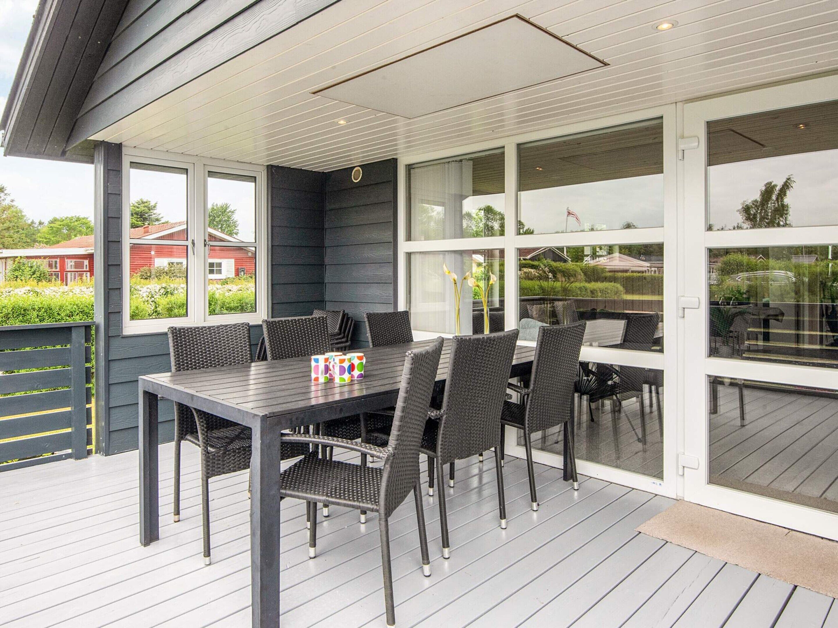 An outdoor patio with a table and chairs, large windows, and a view of the surrounding area.