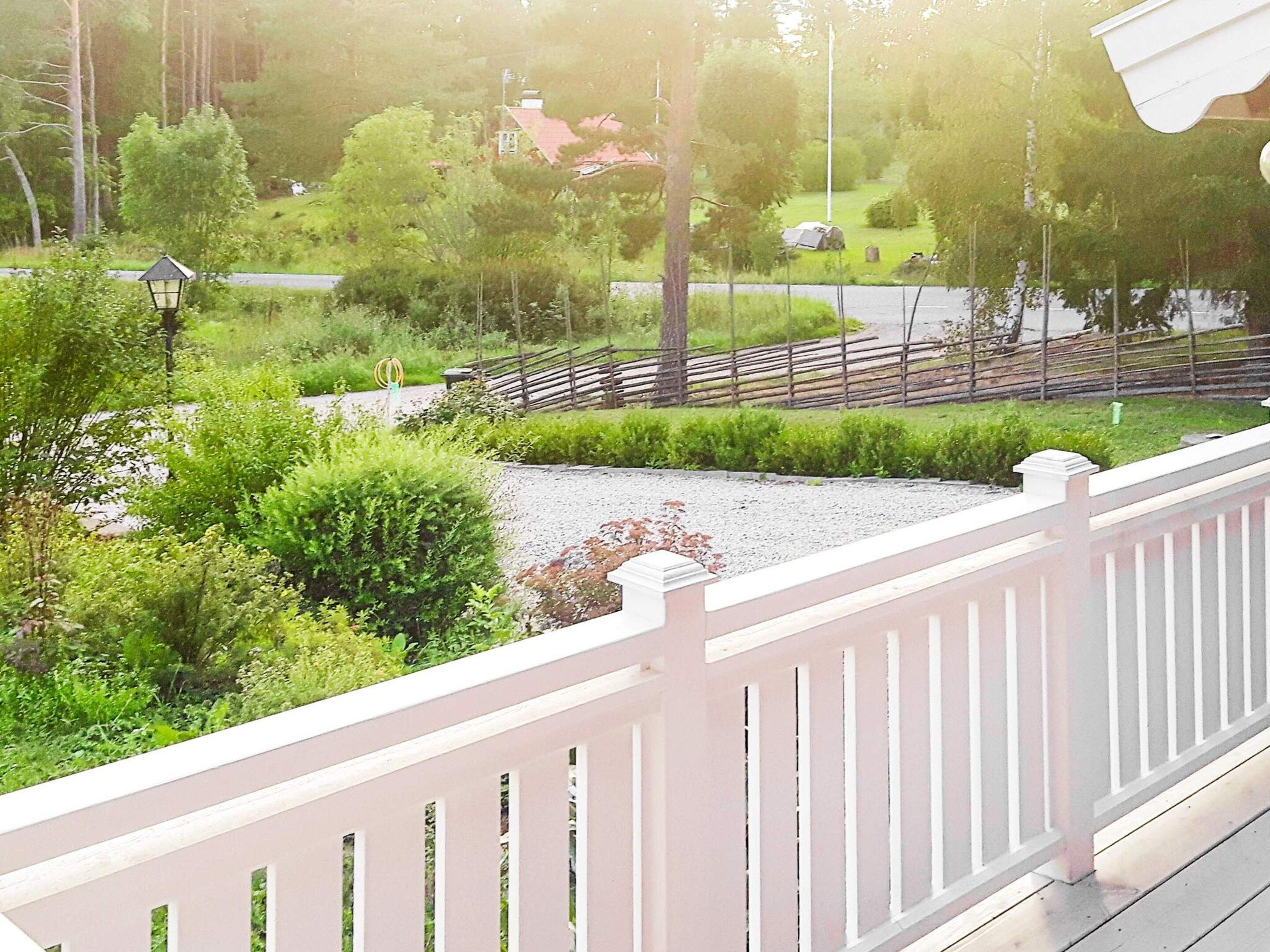 Ein Balkon mit weißer Brüstung, der auf einen angelegten Garten mit Kiesweg, Bäumen und Holzzaun blickt.
