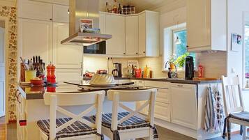 A kitchen with white cabinets, a central island with a kettle, and a dining area with striped chairs.